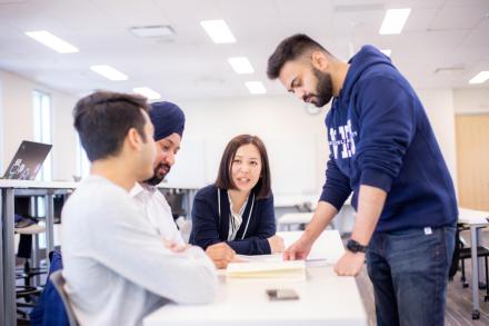 Four students look at a textbook together around a table