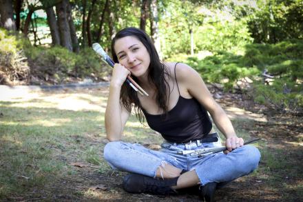 Kashmir Lesnick-Petrovicz sits on the ground and holds paint brushes in her hands.