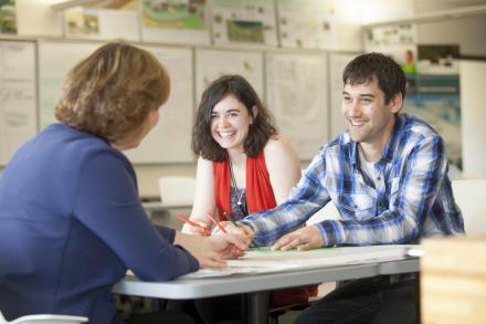 Two graduate students speak with a professor