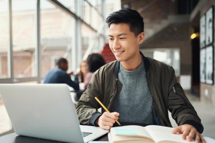 Student looks at a laptop screen and takes notes